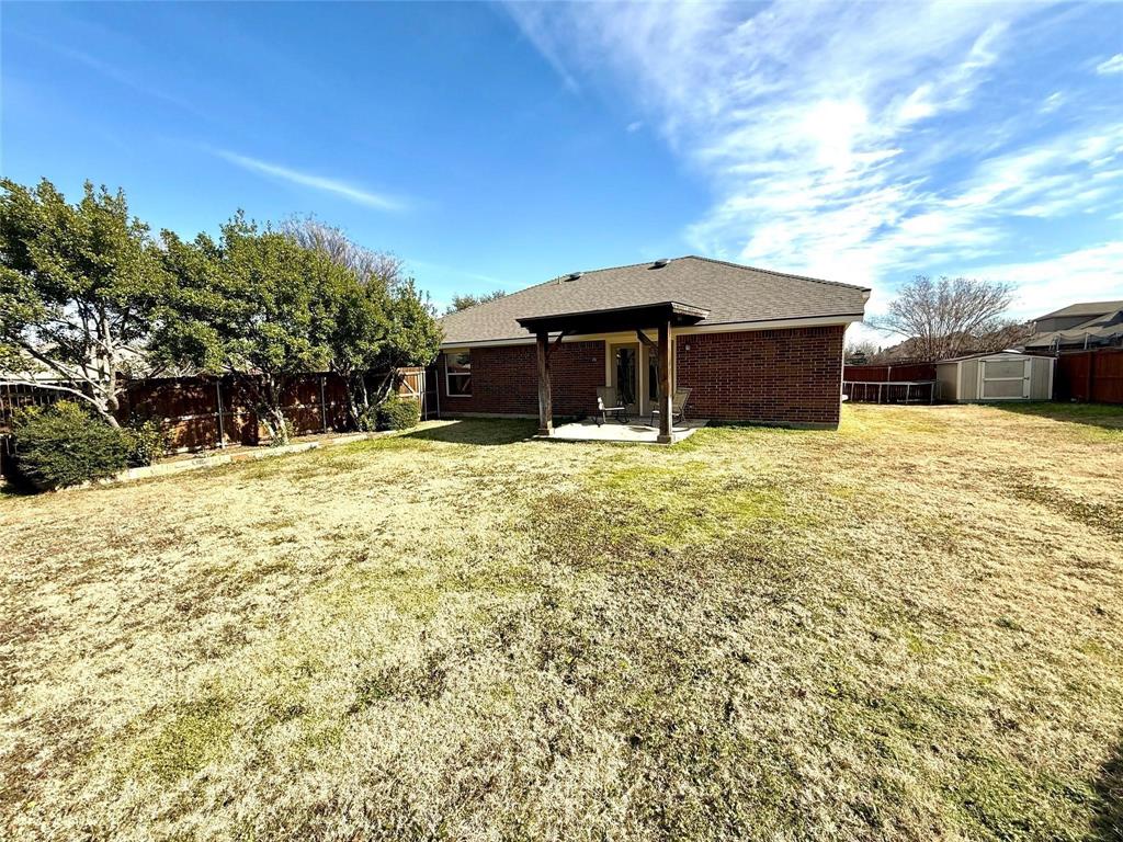 Brick exterior residence featuring a covered patio, pergola, wood fencing, and mature trees