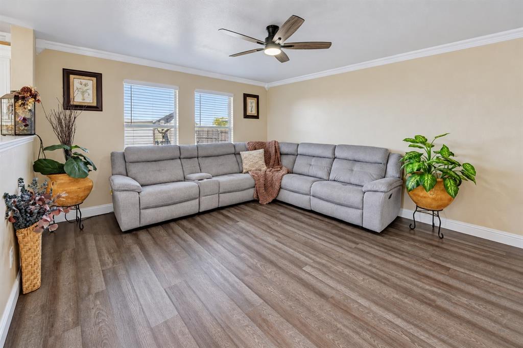 Interior space featuring wood-finish flooring, dual windows with blinds, crown molding, and a ceiling fan with integrated lighting