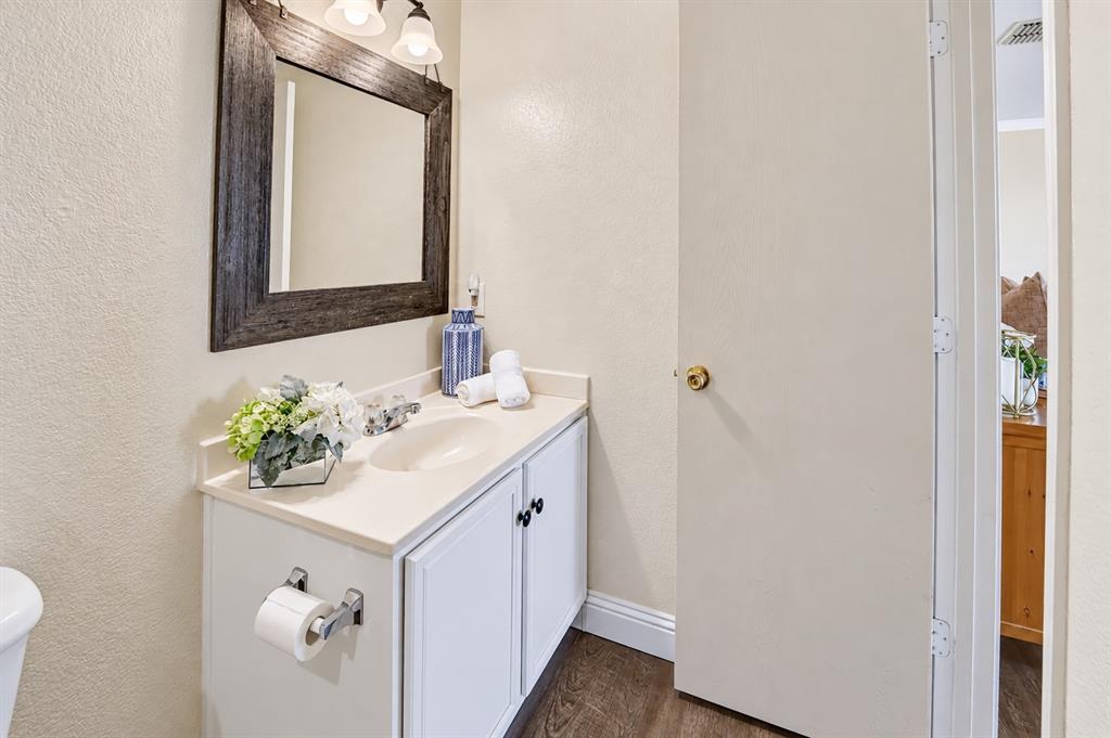 White vanity with a solid-surface countertop and integrated sink, framed rectangular wall mirror, three-light overhead fixture, and wood-finish flooring