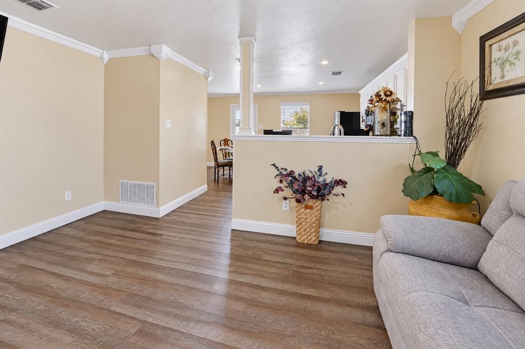 Open-concept interior featuring wood-finish flooring, crown molding, a half-wall partition, and a decorative structural column