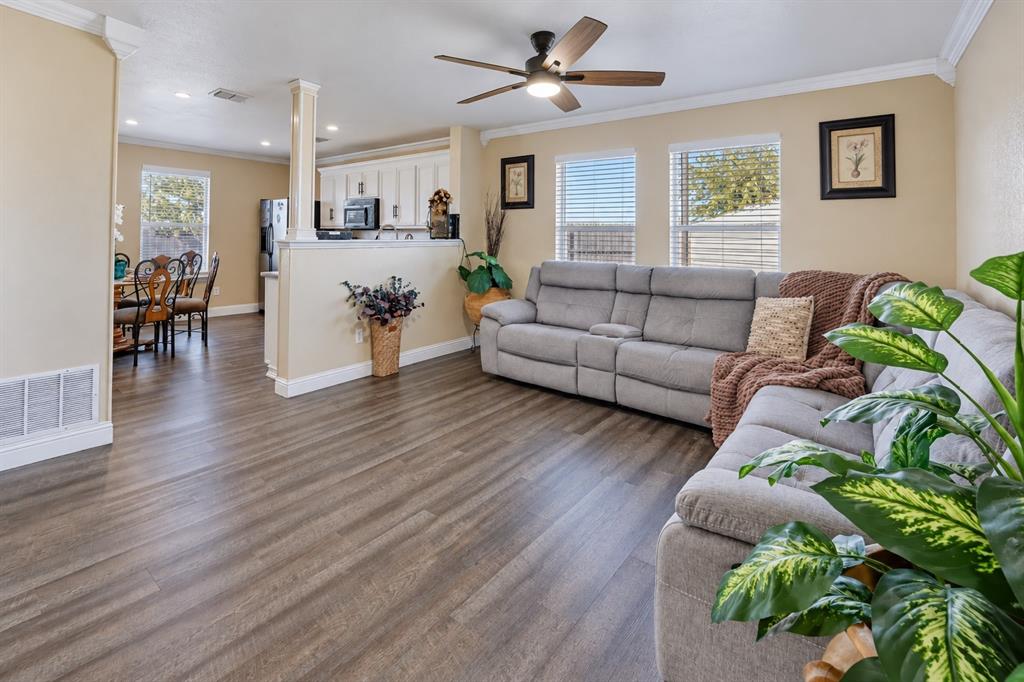 Open-concept area featuring wood-finish flooring, crown molding, a ceiling fan with integrated lighting, and a partial partition wall with a column