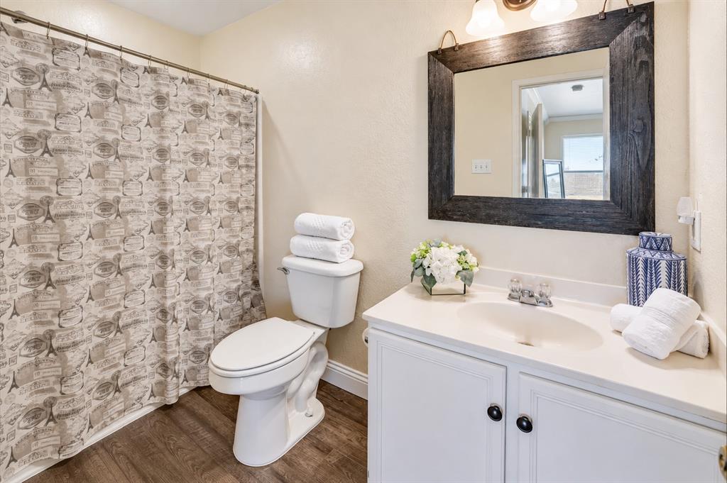 Bathroom featuring a white vanity cabinet with an integrated sink, solid surface countertop, dark-toned wood-finish flooring, and a framed mirror with overhead lighting