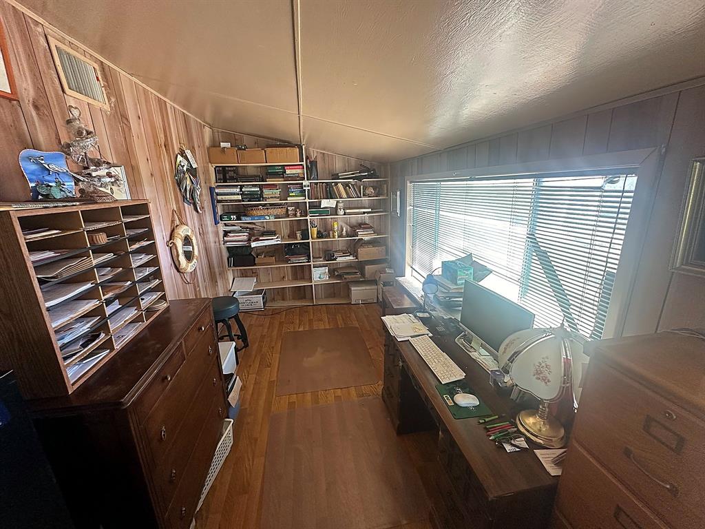 Wood-paneled walls, built-in shelving units, wide horizontal window with blinds, and wood-finish flooring