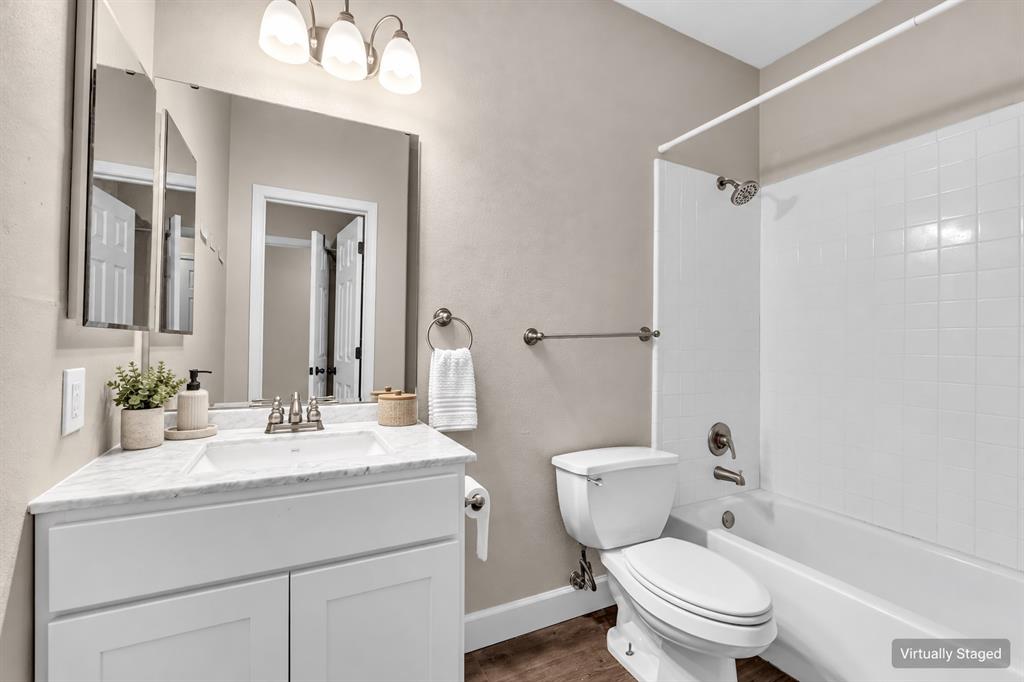 White shaker-style vanity with a stone-finish countertop, undermount sink, three-light vanity fixture, and a white tiled shower surround