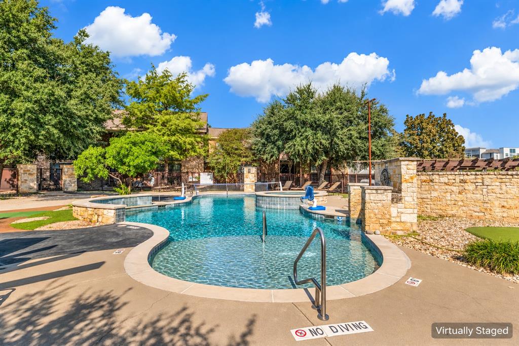 Swimming pool featuring stone-accented perimeter walls, a raised spa, tanning ledge with metal handrails, and surrounding concrete decking Swimming pool featuring stone-accented perimeter walls, a raised spa, tanning ledge with metal handrails, and surrounding concrete decking