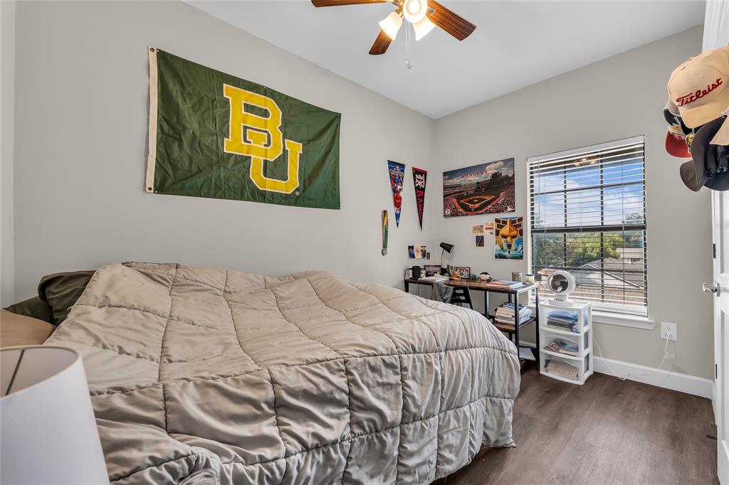Neutral-toned interior room featuring wood-finish flooring, a multi-blade ceiling fan with integrated lighting, and a window with horizontal blinds