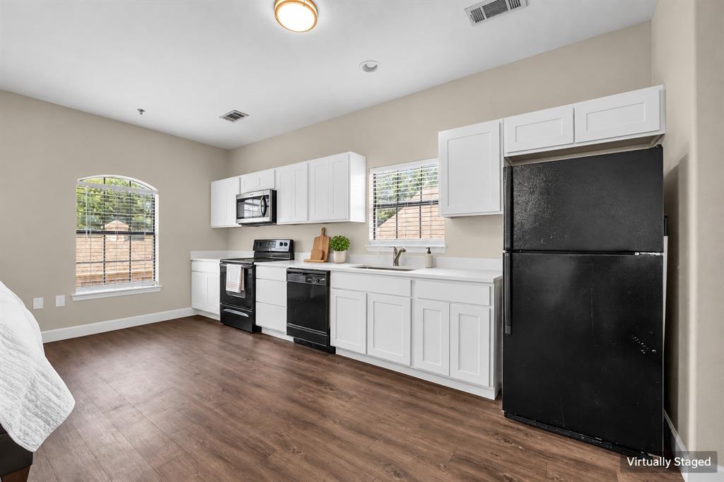Kitchen featuring white cabinetry, solid-surface countertops, black appliances, and wood-finish flooring