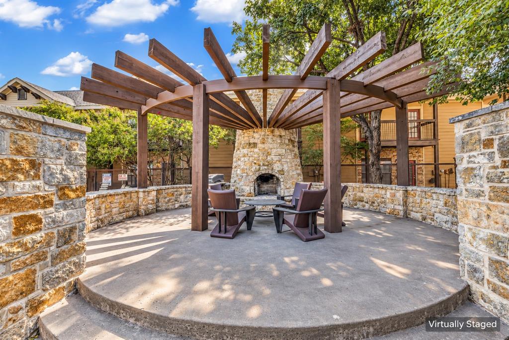 Outdoor patio featuring a circular stone masonry fireplace, a wooden pergola, and stone perimeter walls