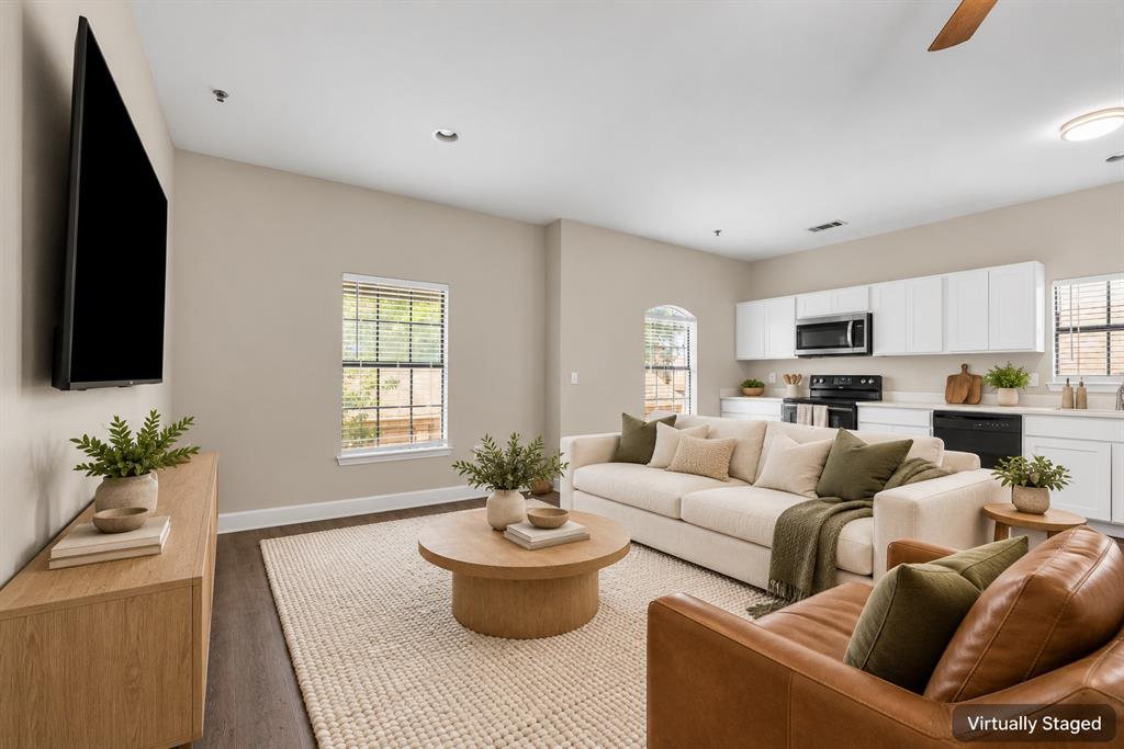 Open-concept living space featuring wood-finish flooring, recessed lighting, white cabinetry, integrated appliances, and arched windows