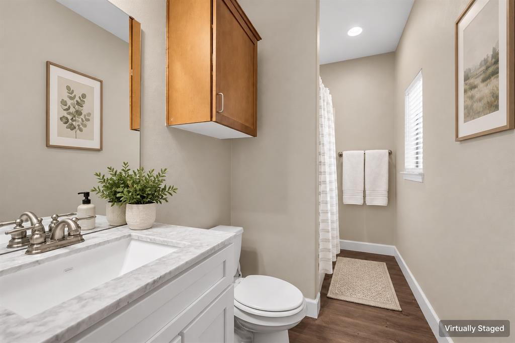 Bathroom featuring a vanity with a stone-finish countertop, undermount sink, dual-handle faucet, wall-mounted wood cabinet, and wood-finish flooring