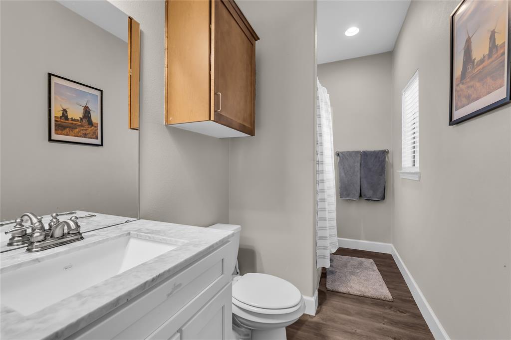 Bathroom featuring a white vanity cabinet with stone-finish countertop, undermount sink, dual-handle faucet, wood-finish flooring, and wall-mounted cabinetry