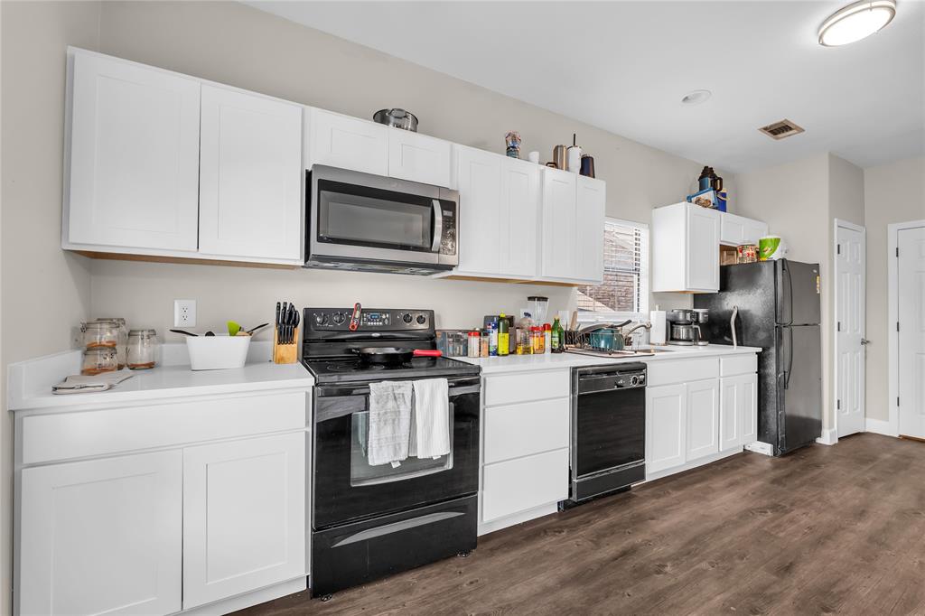 Kitchen featuring white cabinetry, solid surface countertops, wood-finish flooring, and a suite of black appliances including a built-in microwave and range