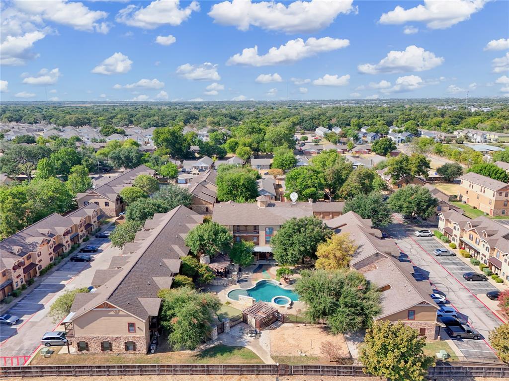 Aerial perspective of multi-family residential complex featuring a swimming pool, attached spa, wooden pergola, and paved parking surfaces Aerial perspective of multi-family residential complex featuring a swimming pool, attached spa, wooden pergola, and paved parking surfaces