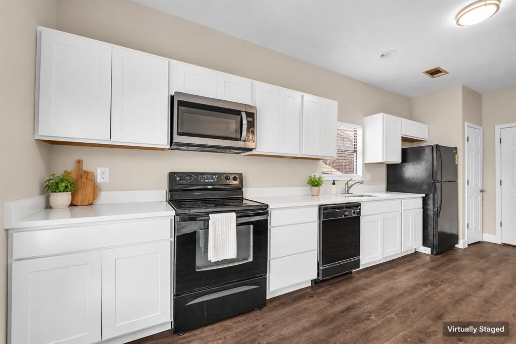 Kitchen featuring white shaker-style cabinetry, solid-surface countertops, wood-finish flooring, and black appliances