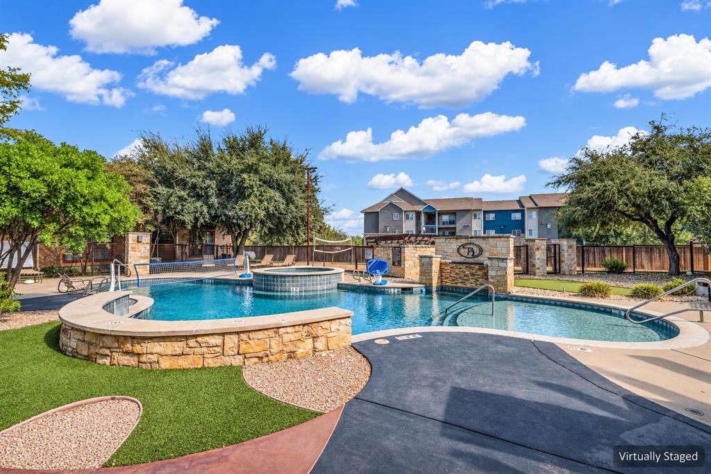 Swimming pool featuring stone-clad retaining walls, an integrated hot tub, a built-in water feature, and a concrete deck Swimming pool featuring stone-clad retaining walls, an integrated hot tub, a built-in water feature, and a concrete deck