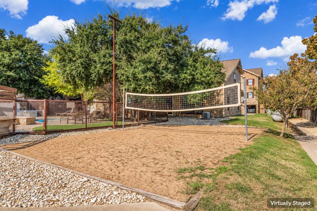 Sand volleyball court featuring a permanent net system, gravel perimeter, and metal fencing