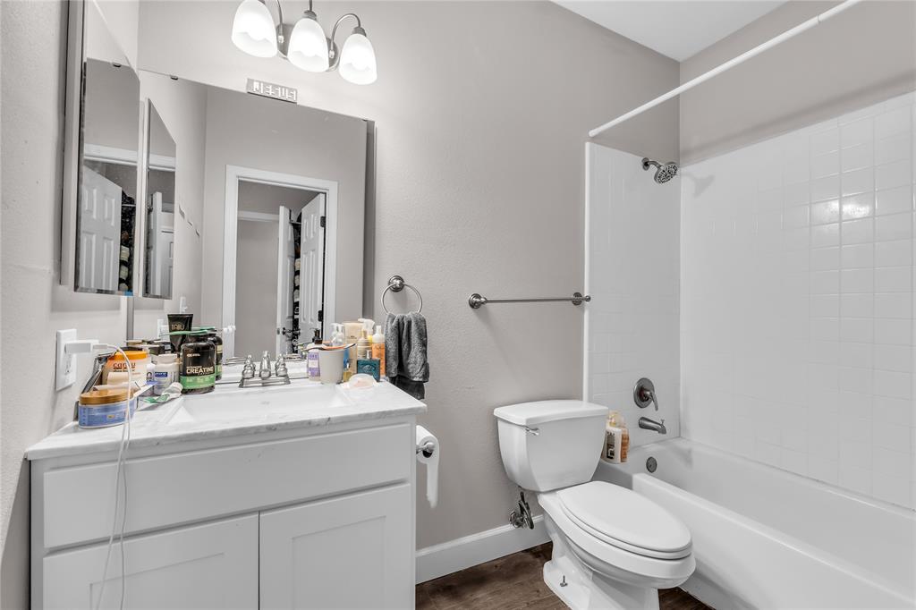 Bathroom featuring a white vanity with a stone countertop, an undermount sink, a framed wall mirror, a three-light fixture, and a tub-shower combination with white wall tile