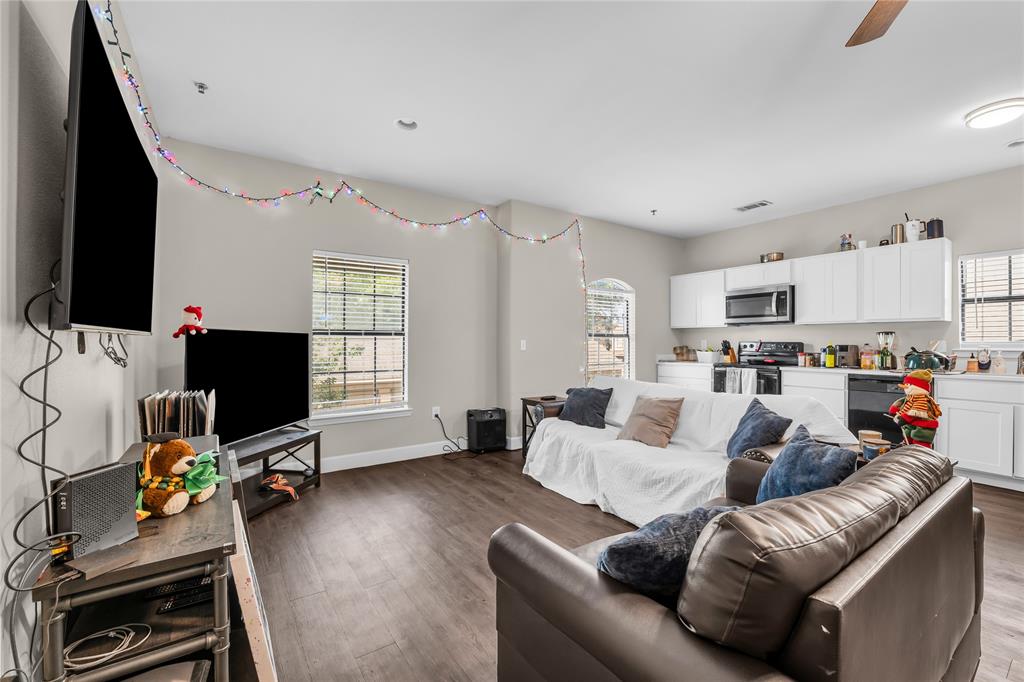 Open-concept living space featuring wood-finish flooring, recessed lighting, and white kitchen cabinetry with integrated appliances