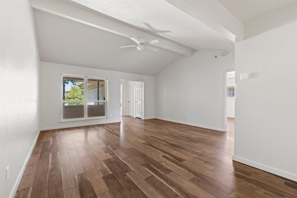 Vaulted ceilings with exposed structural beams, wood-finish flooring, and a ceiling-mounted fan
