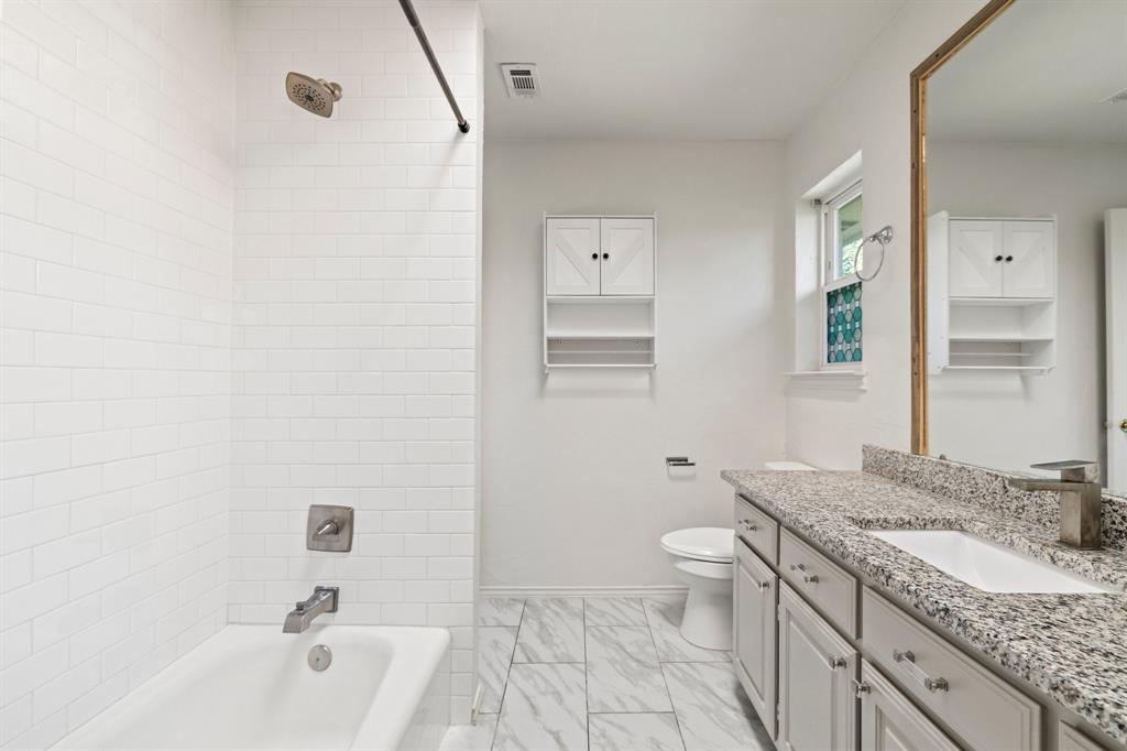 Bathroom featuring a white subway tile surround, stone-composite countertop, undermount sink, shaker-style vanity cabinetry, and patterned floor tile
