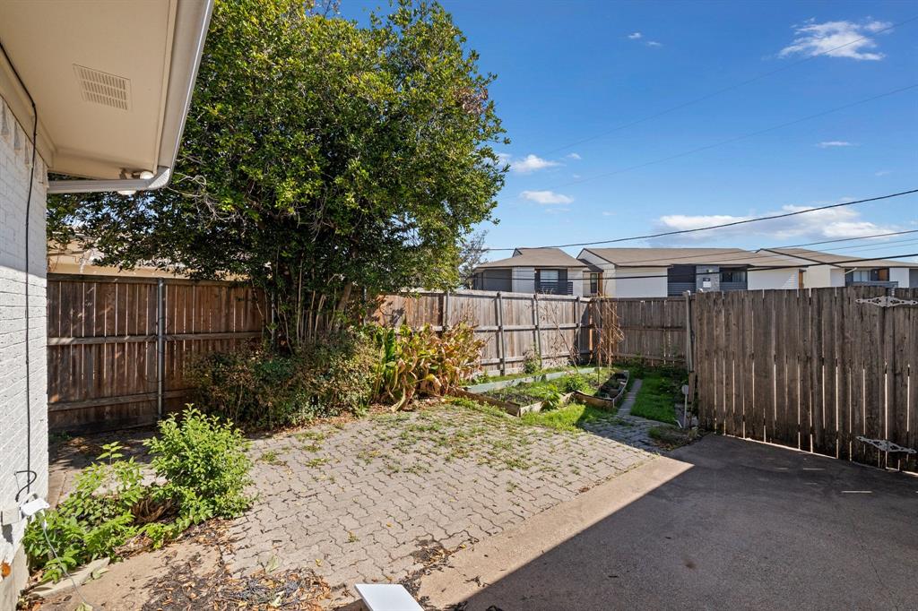 Backyard featuring a paved patio, wood privacy fencing, mature trees, and designated gardening areas