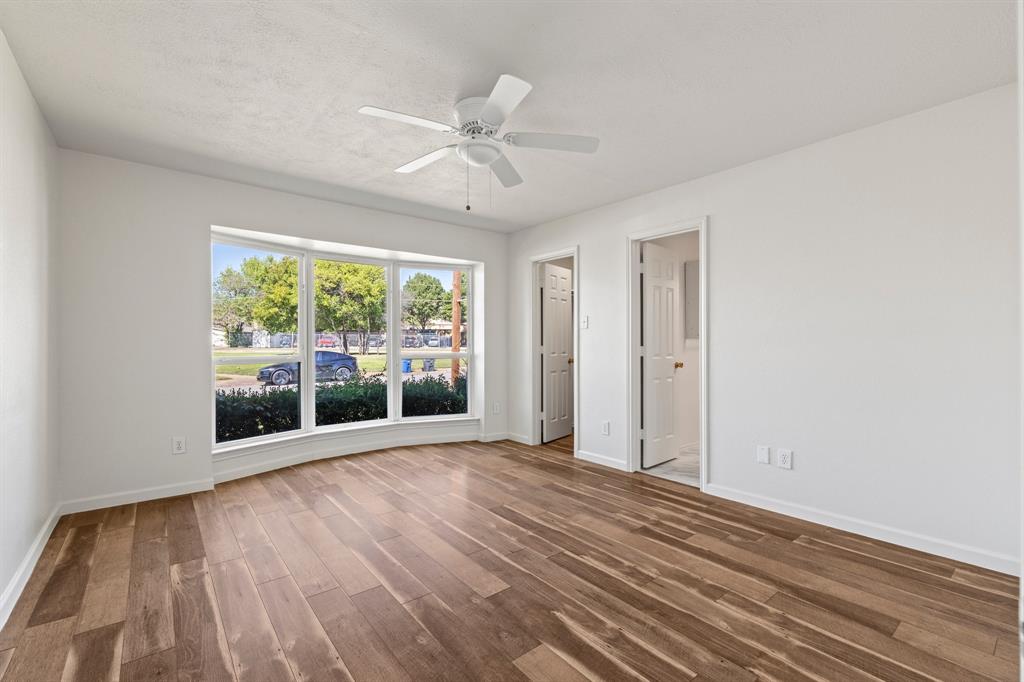Interior space featuring wood-finish flooring, a multi-pane bay window, and a white ceiling fan with integrated lighting