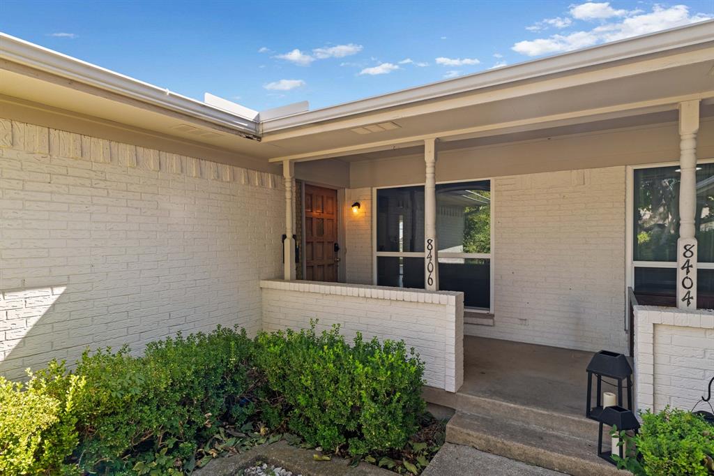 Painted brick exterior featuring a covered front porch, recessed entryway, custom wood-panel front door, and manicured shrubs
