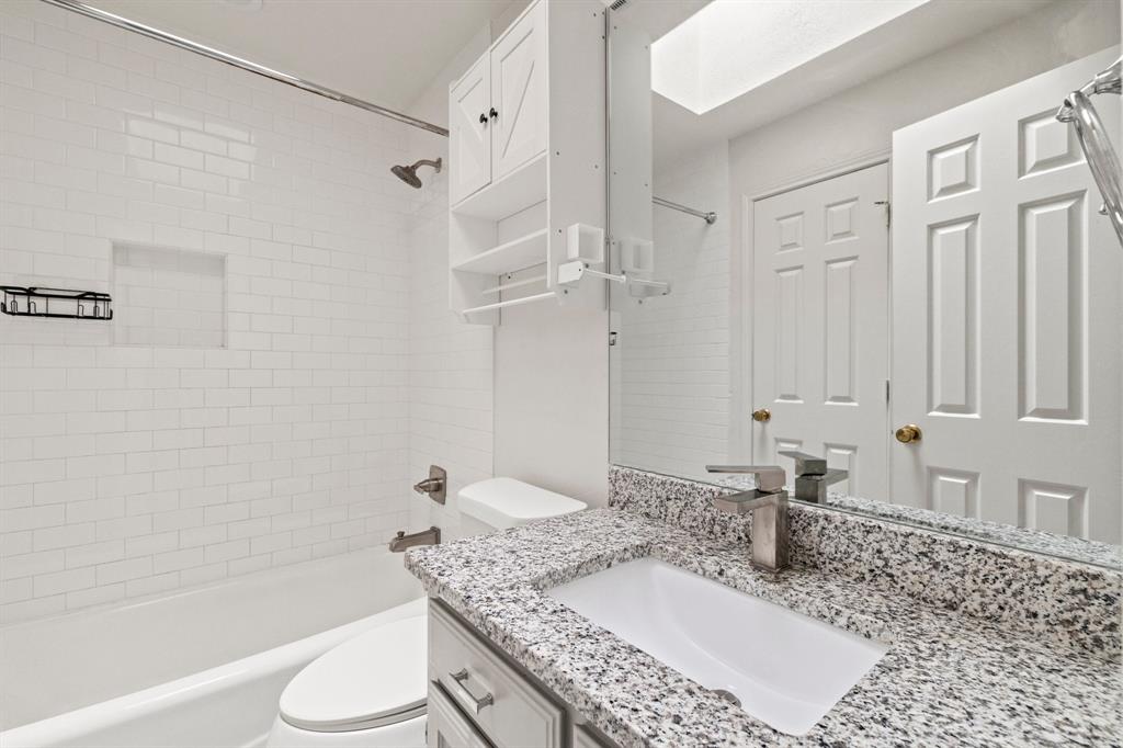 Bathroom featuring subway tile shower surround with integrated recessed niche, stone-finish countertop with undermount sink, built-in cabinetry, and wall-mounted vanity mirror