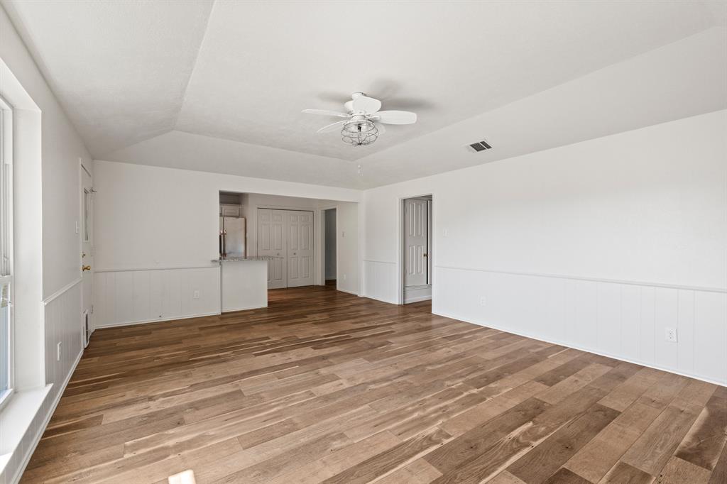 Living area featuring wood-finish flooring, vaulted ceiling with a central paddle fan, wainscoting, and a breakfast bar