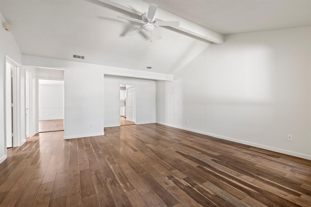 Vaulted ceiling with an exposed beam, wood-finish flooring, and a central ceiling fan
