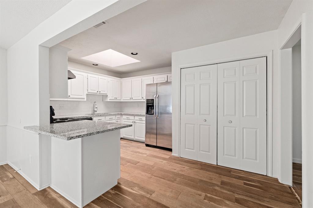 Kitchen featuring white cabinetry, stone countertops, stainless steel refrigerator, skylight, and wood-finish flooring