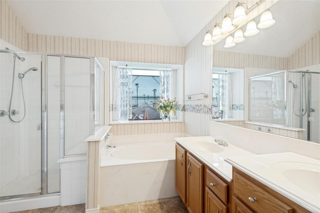 Bathroom featuring a dual-sink vanity with wood cabinetry, a built-in soaking tub, a glass-enclosed shower, and a large vanity mirror with multi-bulb overhead lighting