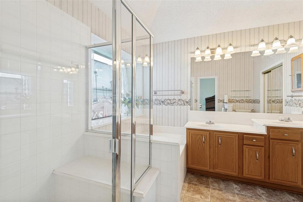 Bathroom featuring a glass-enclosed shower with tiled surround, a built-in soaking tub, a double-sink vanity with wood-finish cabinetry, and a large wall-mounted mirror