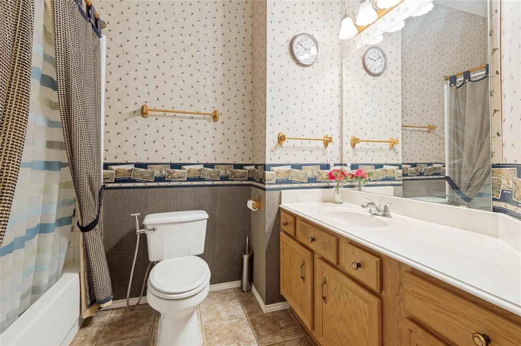 Bathroom featuring a wood vanity with integrated countertop, large wall-mounted vanity mirror, tub with shower surround, tile flooring, and metallic hardware accents