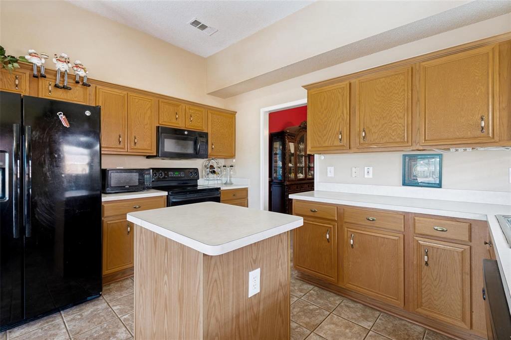 Kitchen featuring natural-finish wood cabinetry, a central island, solid-surface countertops, and tiled flooring Kitchen featuring natural-finish wood cabinetry, a central island, solid-surface countertops, and tiled flooring