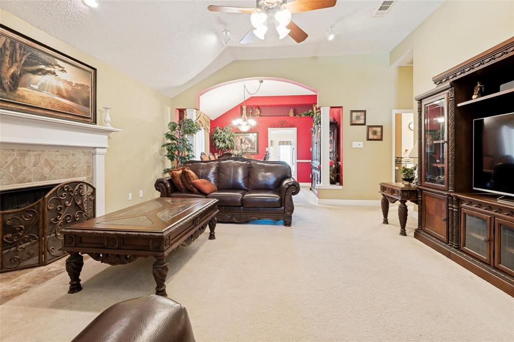 Living area featuring a vaulted ceiling, fireplace with tile surround, decorative mantel, archway with architectural columns, and ceiling fan Living area featuring a vaulted ceiling, fireplace with tile surround, decorative mantel, archway with architectural columns, and ceiling fan
