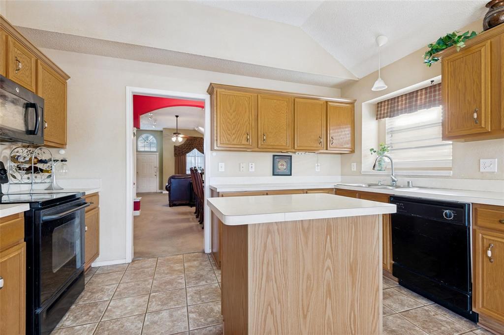 Kitchen featuring oak-finish cabinetry, central island with solid-surface countertop, tiled flooring, and vaulted ceiling Kitchen featuring oak-finish cabinetry, central island with solid-surface countertop, tiled flooring, and vaulted ceiling