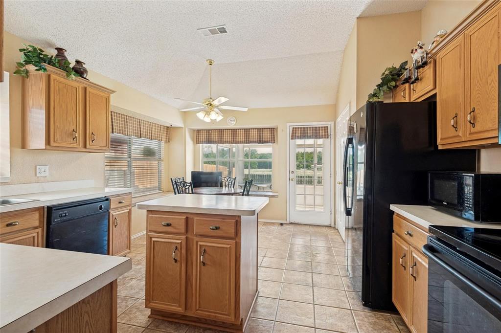 Kitchen featuring oak cabinetry, a central prep island, tile flooring, vaulted ceilings, and a light-filled breakfast nook