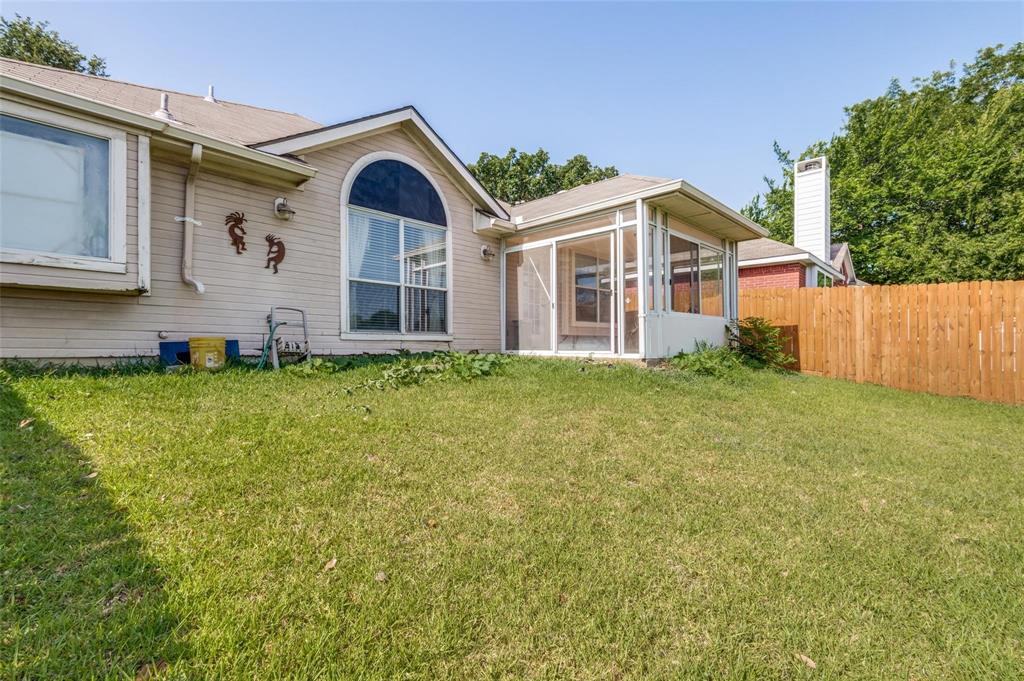 Rear exterior featuring a screened-in sunroom, arched picture window, chimney, and wood privacy fencing