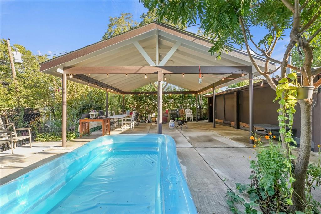 Covered outdoor patio with a gable roofline, exposed wooden support beams, concrete flooring, and attached string lighting