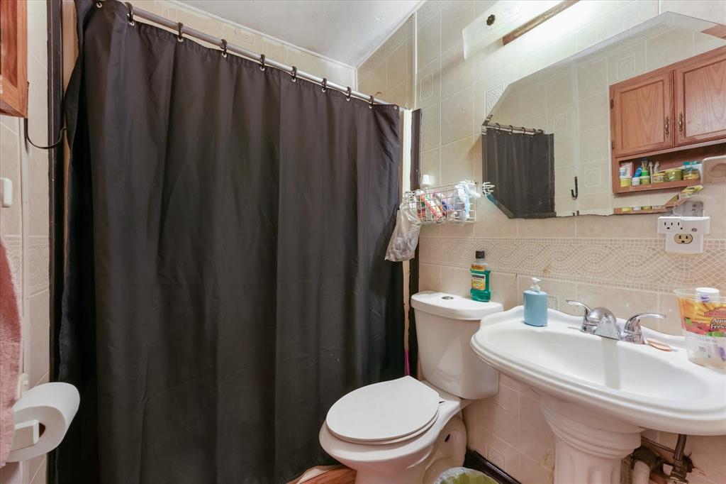 Bathroom featuring wall-to-wall ceramic tiling, a pedestal sink with dual-handle chrome faucet, a wall-mounted medicine cabinet with wood-finish cabinetry, and a large beveled-edge mirror