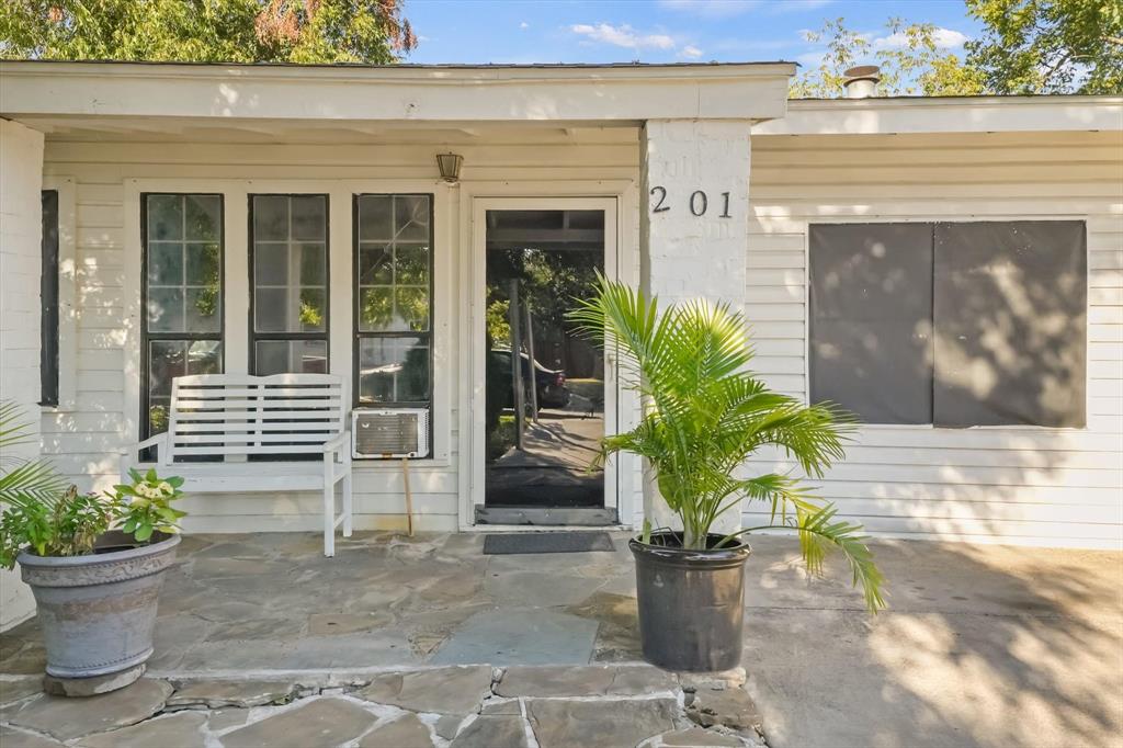 Exterior facade featuring painted horizontal siding, stone-paved front patio, multi-pane windows, and a glass-paneled entry door Exterior facade featuring painted horizontal siding, stone-paved front patio, multi-pane windows, and a glass-paneled entry door