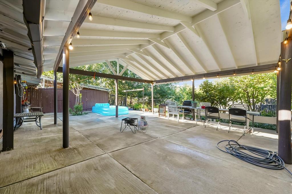 Covered patio featuring a vaulted ceiling with exposed beams, concrete flooring, and metal support posts