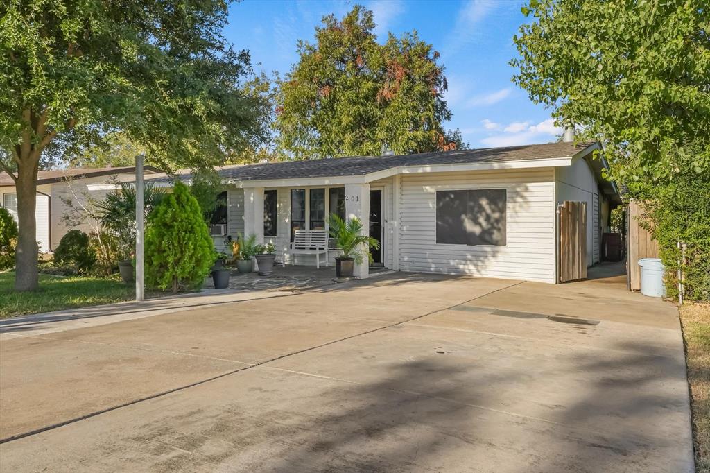 Single-story exterior featuring white horizontal siding, a concrete driveway, a covered front porch, and mature trees Single-story exterior featuring white horizontal siding, a concrete driveway, a covered front porch, and mature trees