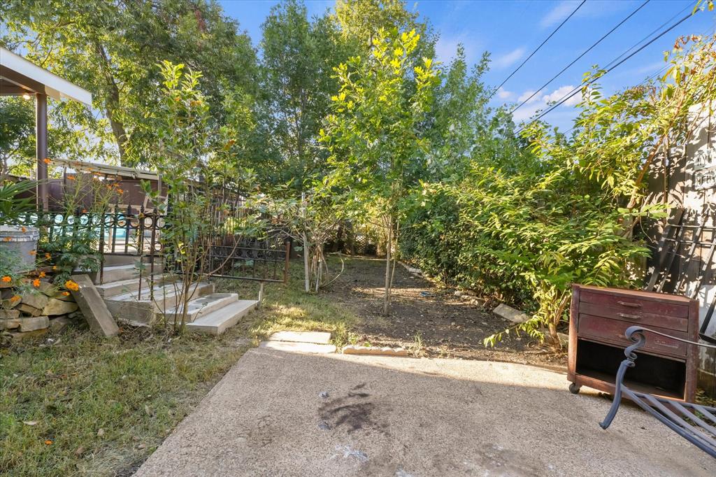 Concrete patio with stone retaining wall, decorative metal railing, and mature trees