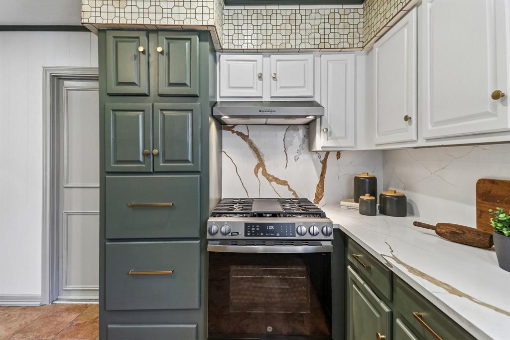 Two-tone cabinetry with brass hardware, stainless steel range with integrated cooktop, white countertop, and patterned tile backsplash