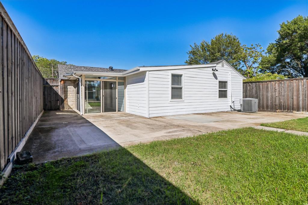 Expansive concrete patio, wood privacy fencing, sliding glass doors, white horizontal siding, and a manicured lawn