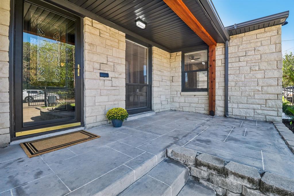 Stone veneer facade, glass-paneled entry door, dark-framed windows, wood beam accents, and a stone patio with integrated steps Stone veneer facade, glass-paneled entry door, dark-framed windows, wood beam accents, and a stone patio with integrated steps