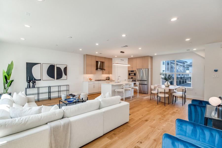 Open-concept interior featuring wood-finish flooring, recessed lighting, and a kitchen equipped with light wood-finish cabinetry, a central island, and stainless steel appliances