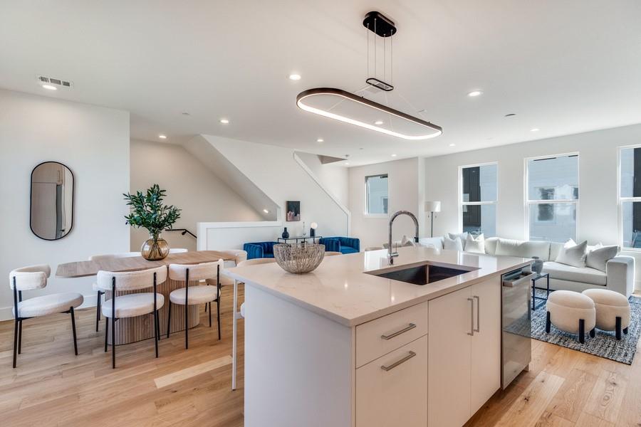 Kitchen island with stone-finish countertop, undermount sink, modern oval-shaped pendant lighting, and wood-finish flooring